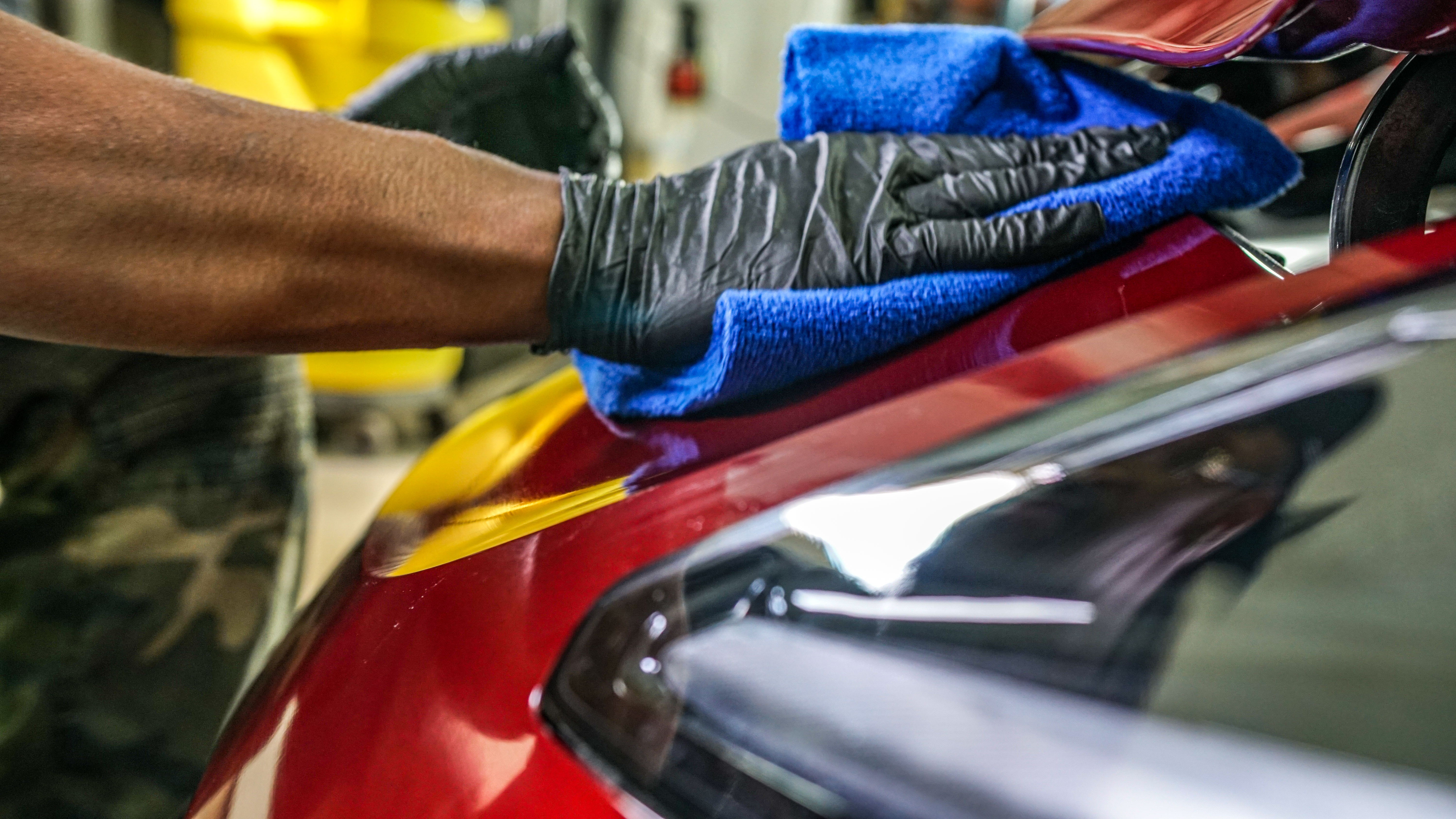 Hand wiping red Corvette hood to a mirror finish
